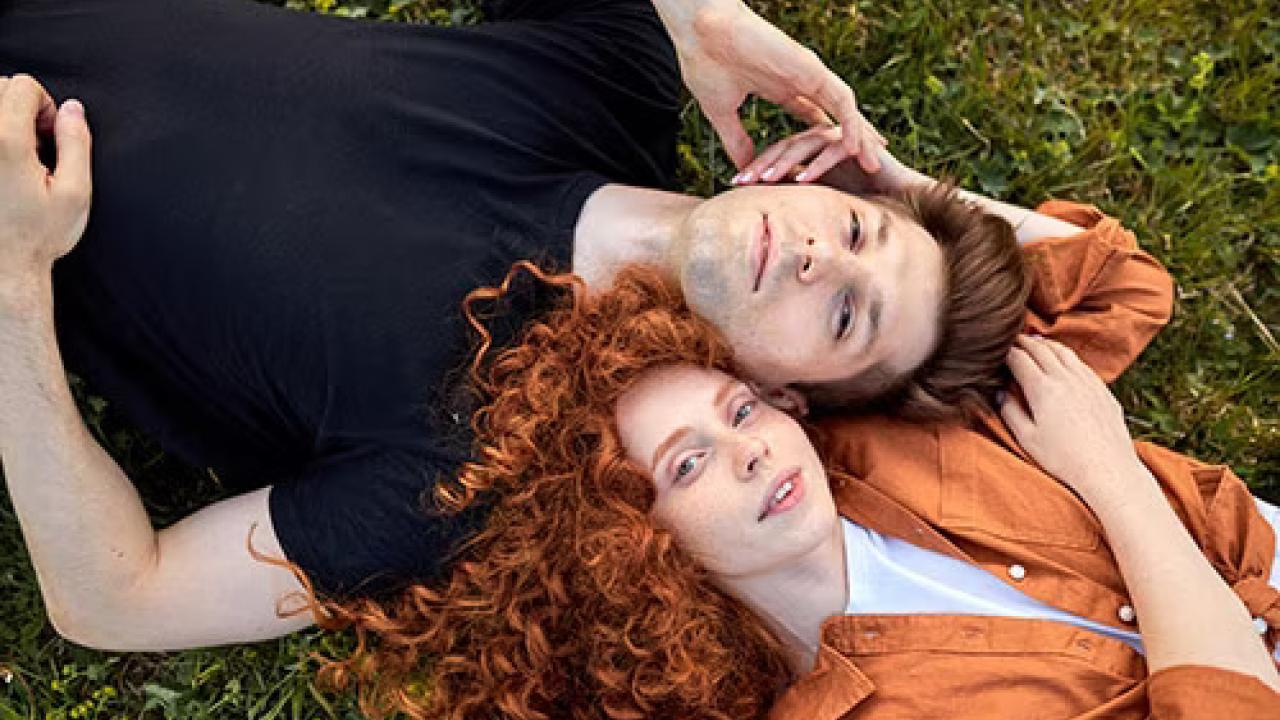 Two people lying with heads together in the grass.