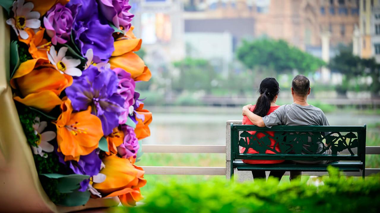 2 people sitting on a bench in front of flowers