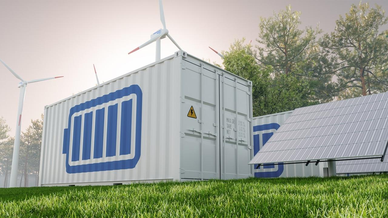 A storage container with a battery symbol on the side, outside next to solar panels and wind turbines.