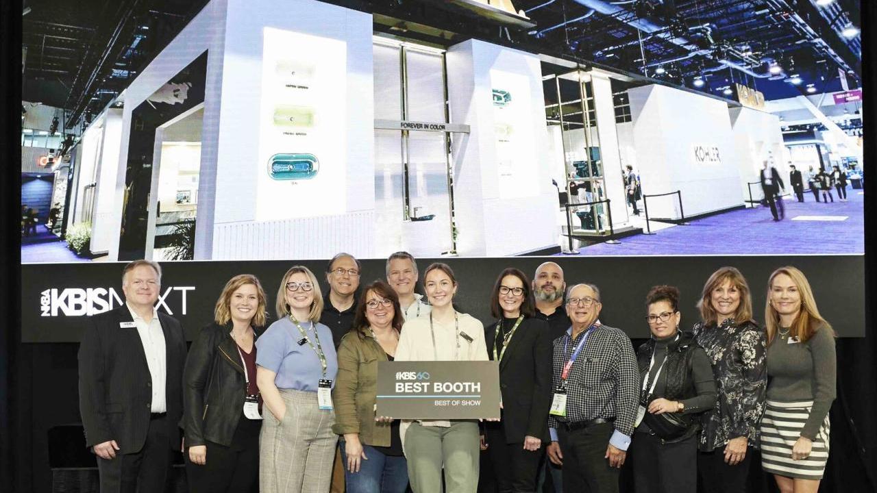 A team of people standing posed in front of the Kohler booth. One holds a sign "Best booth"
