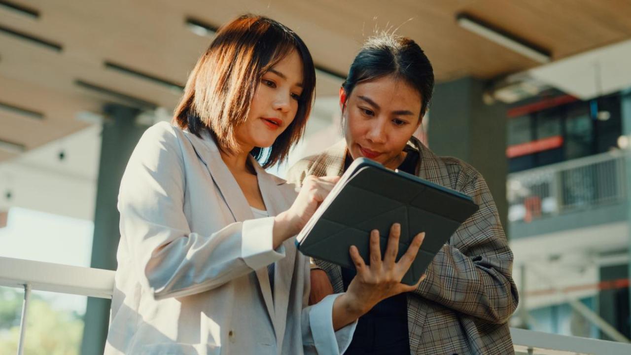 Two standing people looking at a tablet device in a business setting.