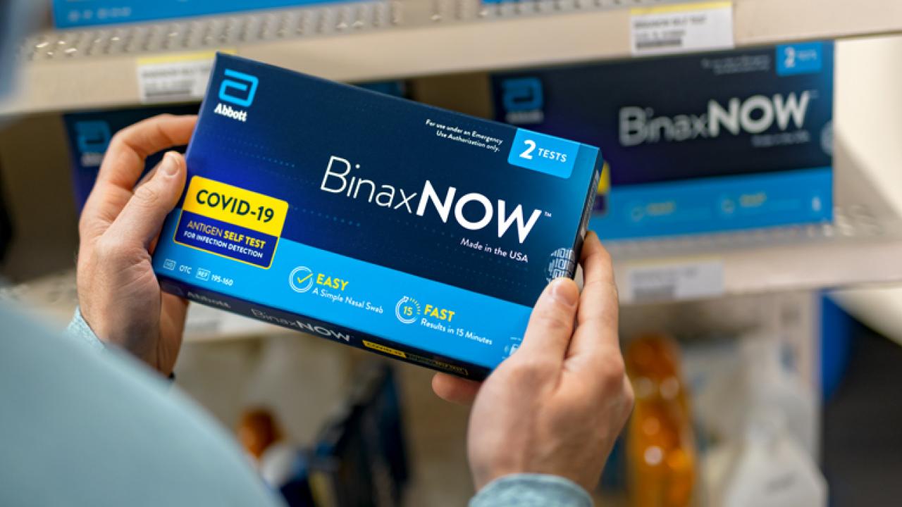 A person holding a BinaxNow Covid-19 test kit. 