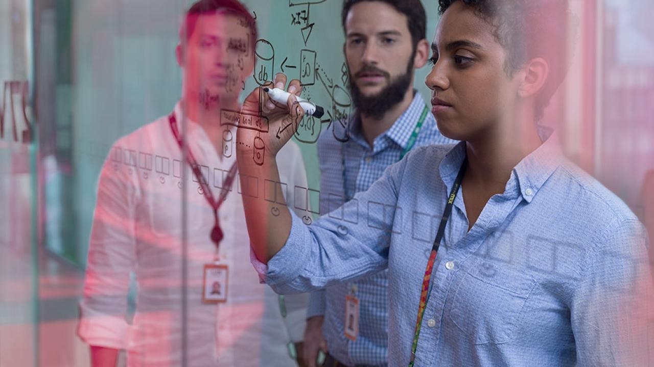 person draws on a white board while two others look on