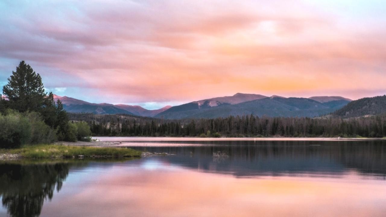 wide river and pine trees at dawn with mountains in the distance