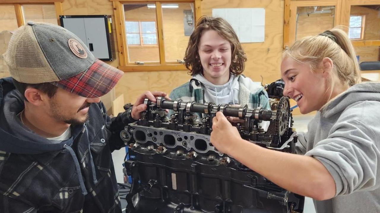 Three smiling people working on a large mechanical piece.