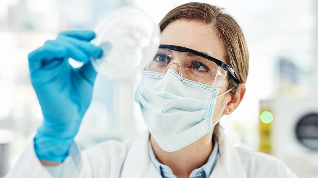 A scientist in protective gear looking at a petri dish