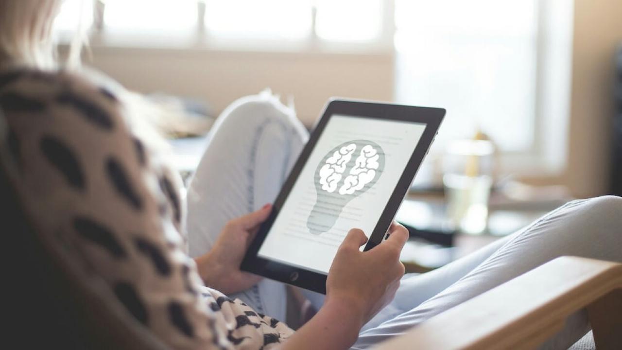 a person holding a tablet, an abstract image of a brain inside a lightbulb on the screen