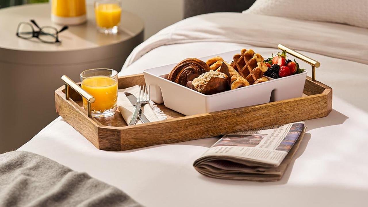A tray filled with breakfast items, a newspaper tucked underneath, placed on a bed.
