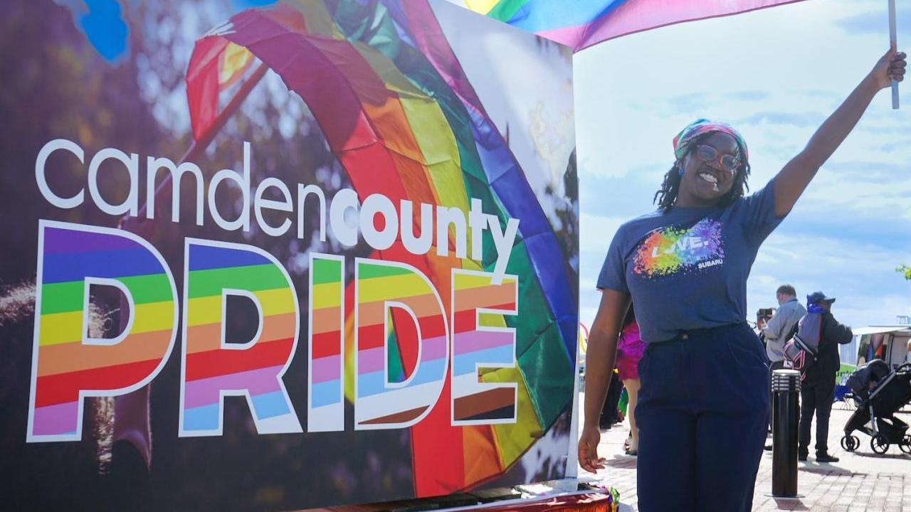 A person waving a pride flag next to a sign that says "Camden County PRIDE"