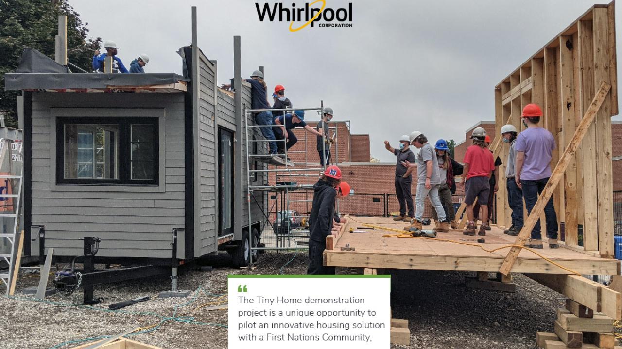 a group of people stand on wood building structure next to a completed tiny house