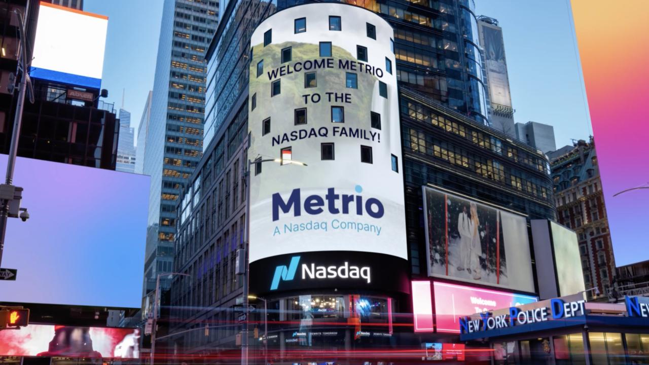 Billboard on the side of a tall building in a busy intersection. Metrio and Nasdaq logos.