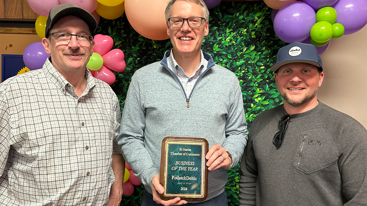 Three smiling people posed with a plaque. Balloons behind them.