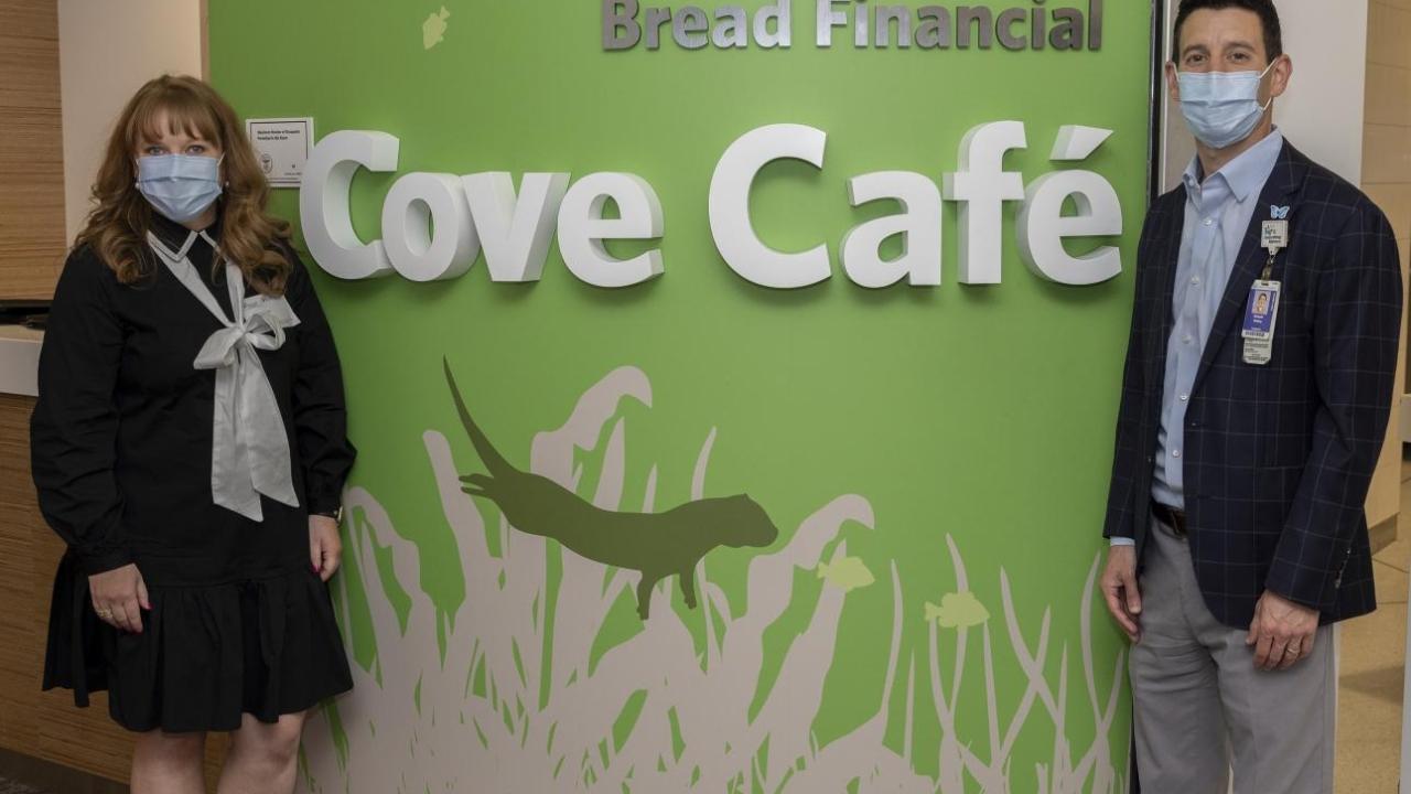 Two people in front of Bread Financial Cove Café sign
