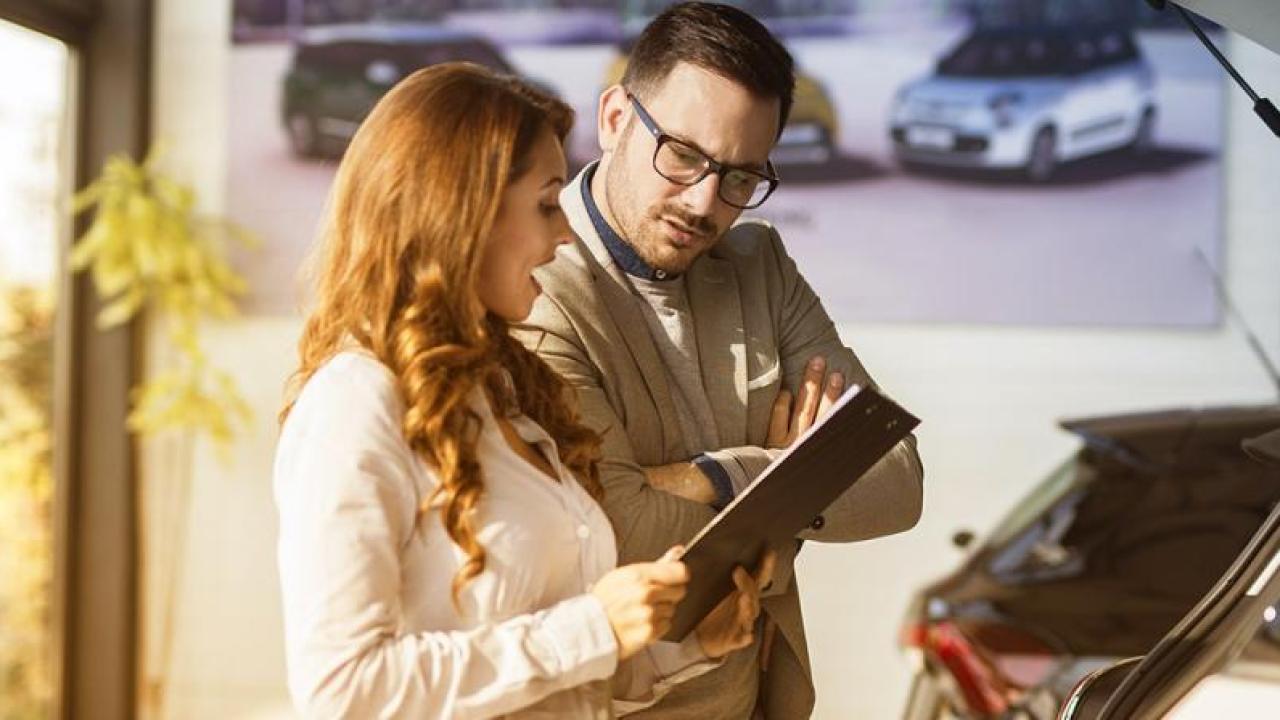 Two people in a car dealership looking at a clipboard.