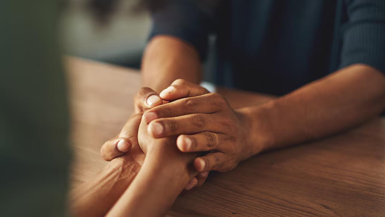 Close up of two people holding hands over a table.