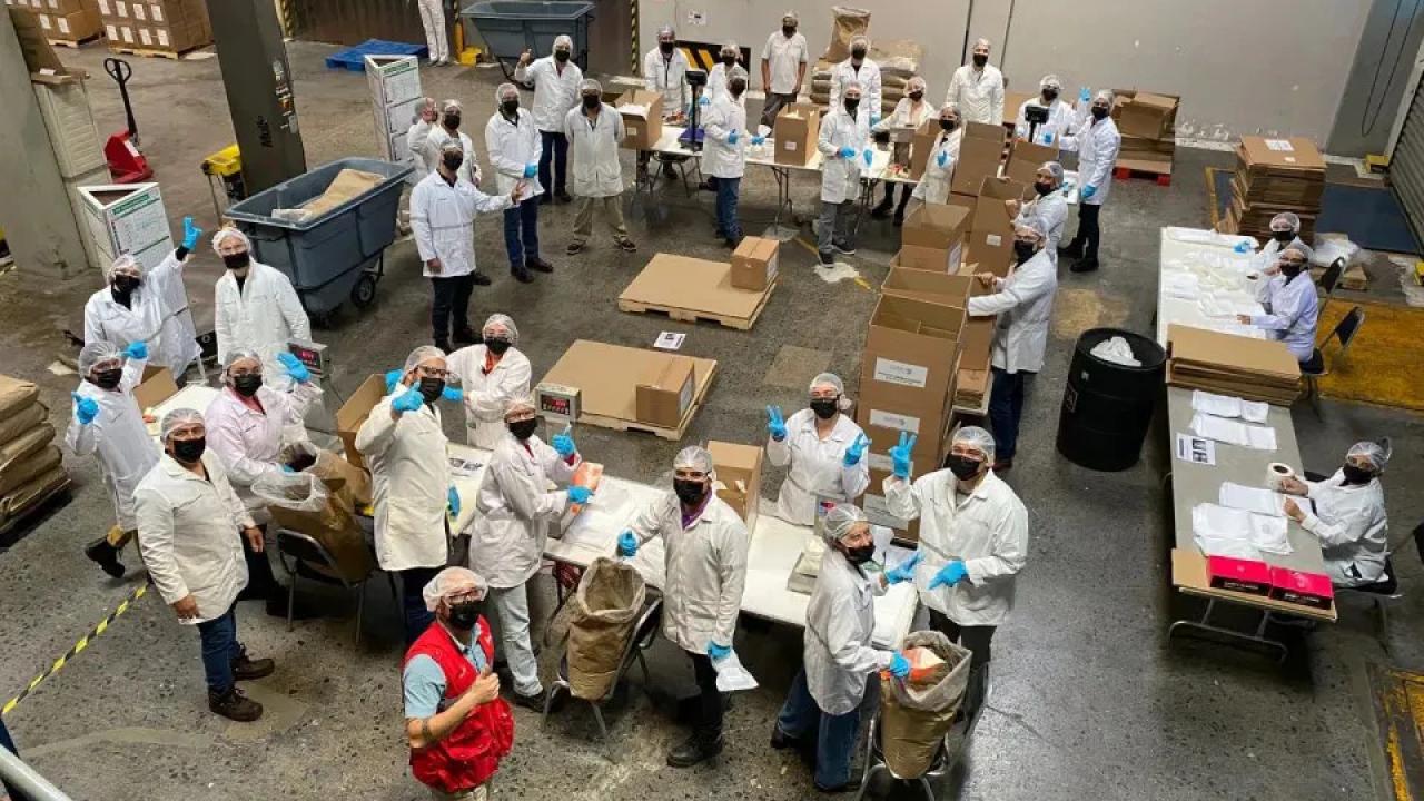 Aerial view of volunteers in protective coverings, working with boxes and food in a warehouse setting.