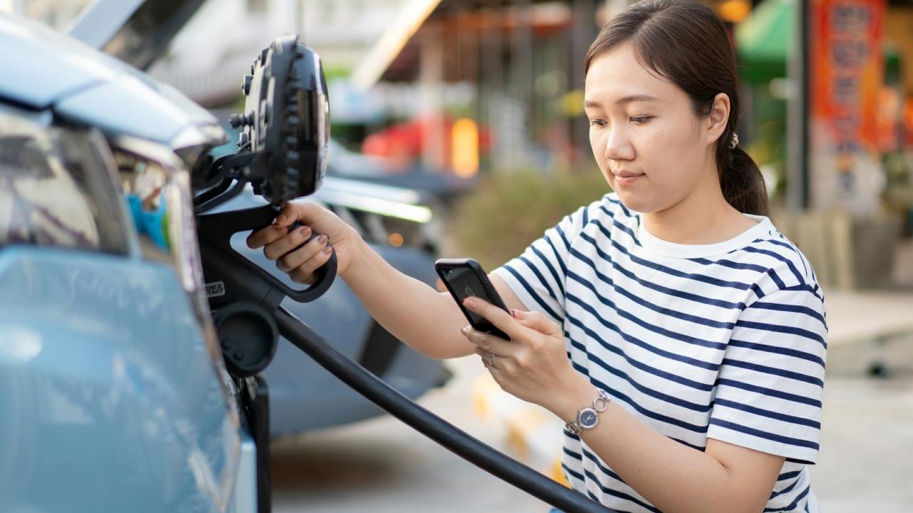 a person looks at their phone while plugging in their vehicle