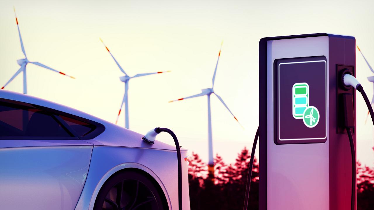 an electric vehicle plugged in to a charging station. Windmills in the background.