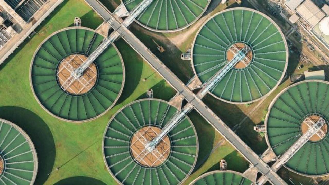 Aerial view of a large treatment plant with many open holding tanks with green substance. 