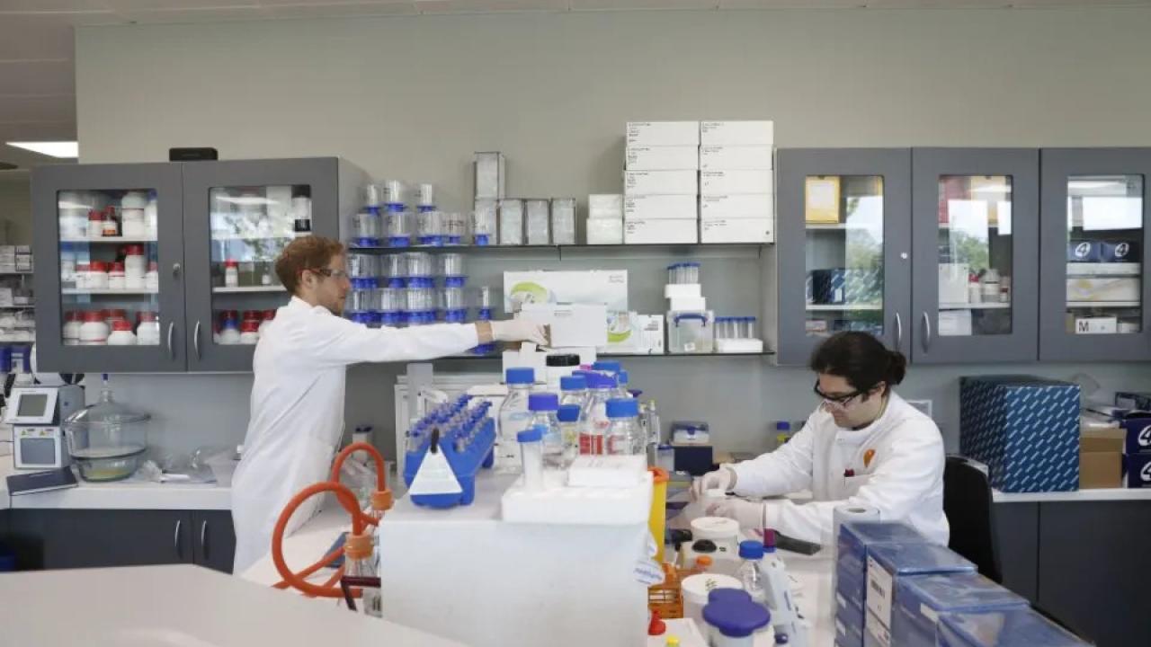 Two people in a laboratory setting wearing protective gear.