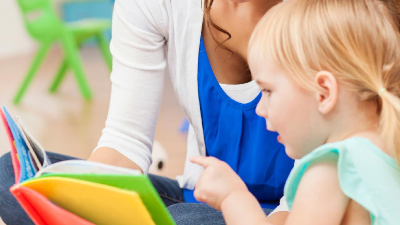 An adult reading a book with a seated child.