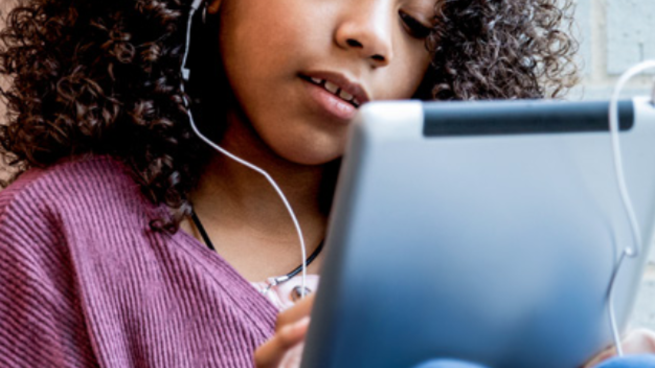 A child using a tablet device with earphones plugged in.