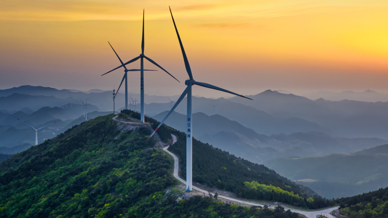Wind turbines on top of a peak, setting sun in the background