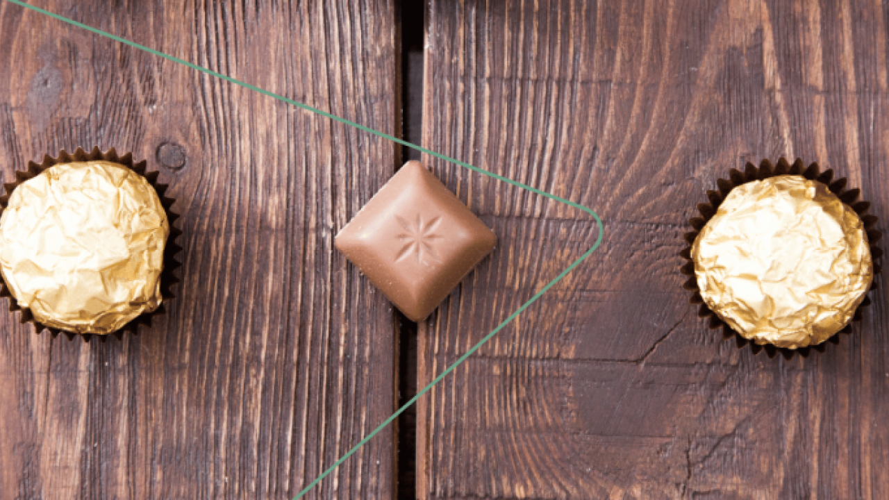 A row of five chocolates on a wood surface.