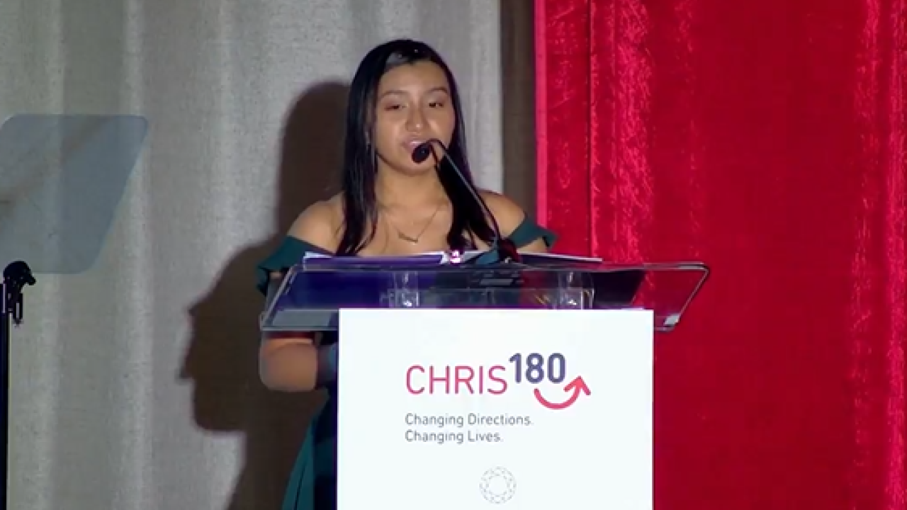 A person speaking at a podium. "CHRIS 180" sign in front.