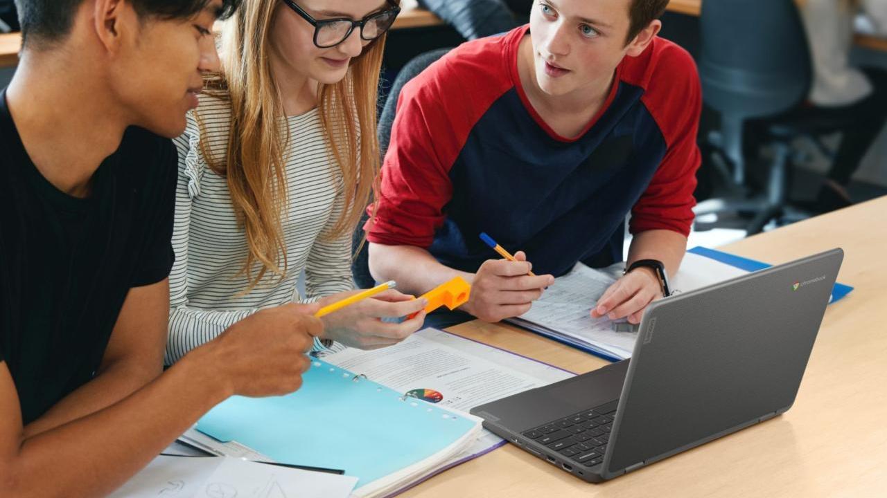 Students working together at a desk, an open laptop between them.