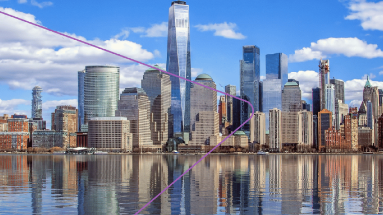 A city skyline, a body of water in front. A partly cloudy blue sky.