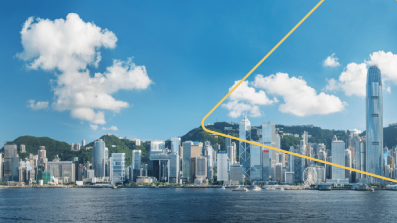 City skyline with an expanse of water in front. A few clouds in a blue sky above.