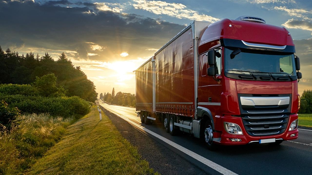 A semitruck driving down a road. A sunset in the background.