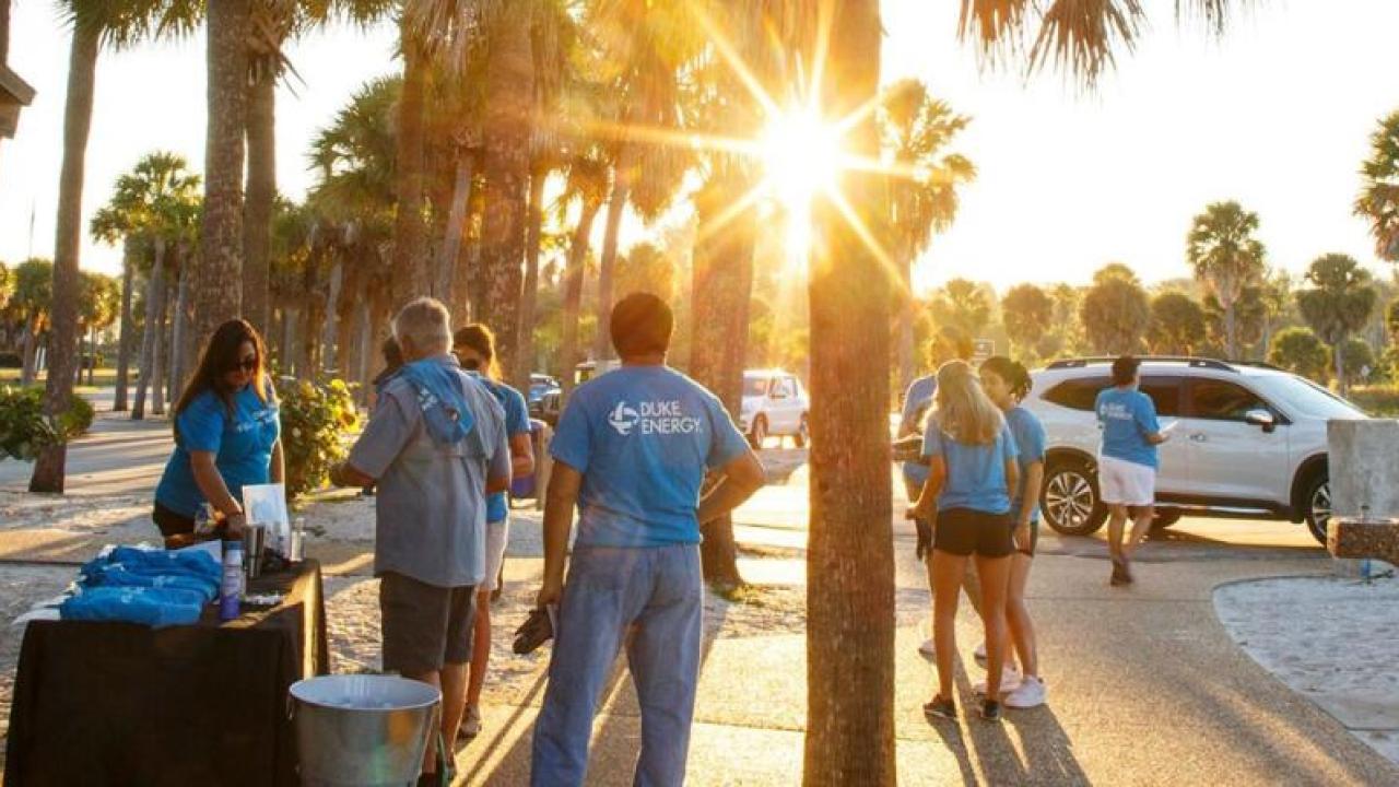 A group of volunteers gathered on a sidewalk in a park setting.
