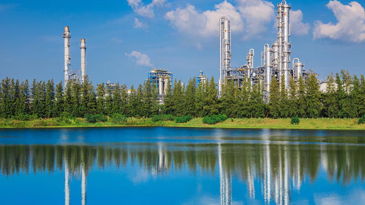 industrial buildings beyond a treeline and pond