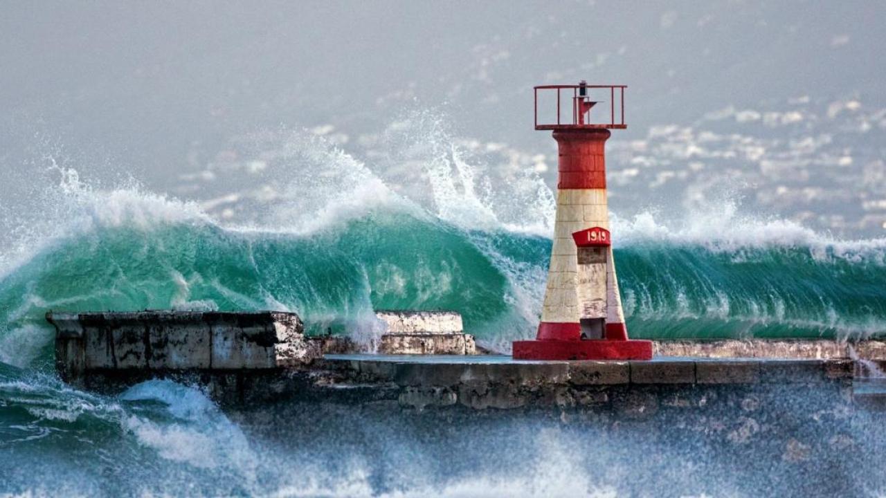 Tall waves crashing over a wall with beacon.