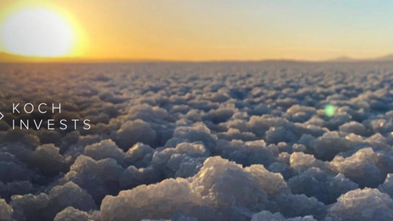 Close up of salt plain, sun rising in the distance. "Koch Invests".
