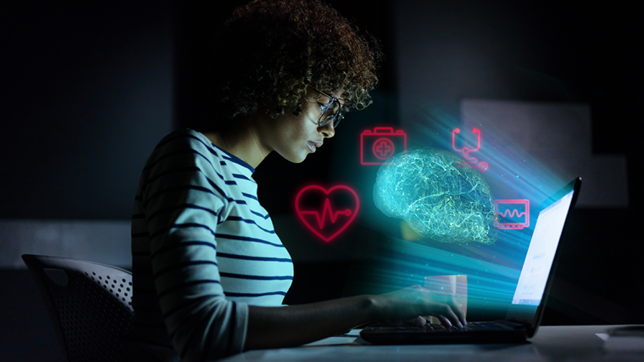person working on laptop in the dark with artistic computer symbols shining from it