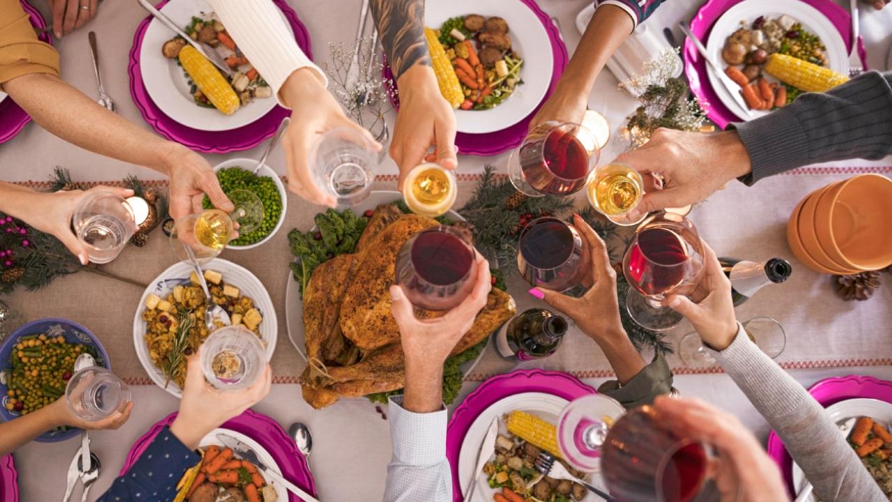 Many hands, each holding a beverage glass, meeting at the center of a table full of different foods.