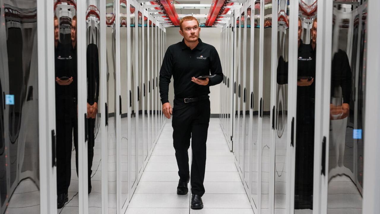 A person walking down a hall lined with large servers on both sides
