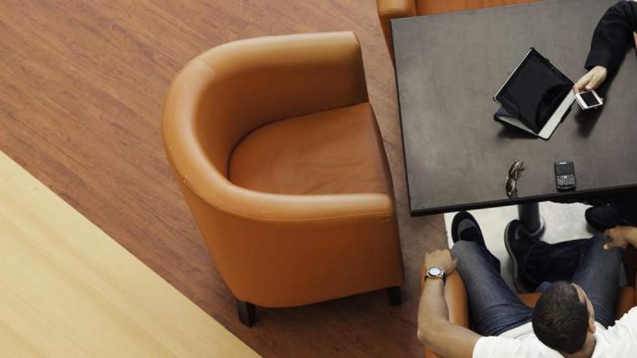 Two people seated in armchairs, a laptop open on a small table in front of them.
