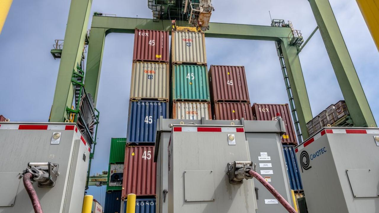 Stacked shipping containers and cranes, power boxes in front.