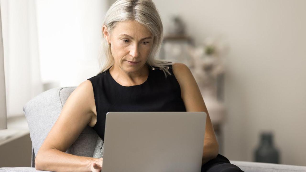 Woman seated at a table reviewing a laptop.
