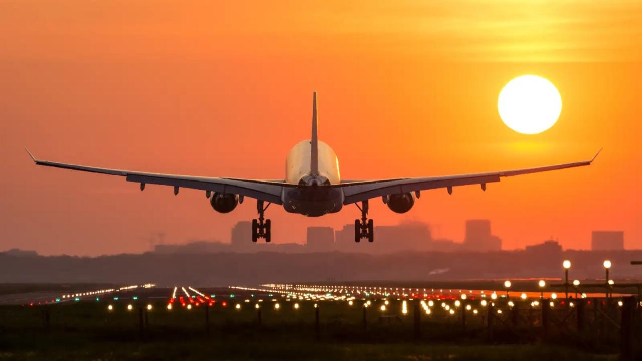 The back of a commercial jet as it takes off towards a setting sun