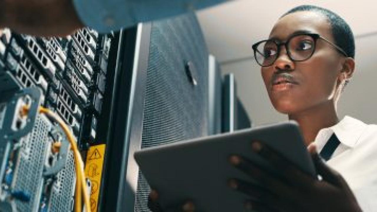 A person holding a tablet, looking at towers of electronic equipment.