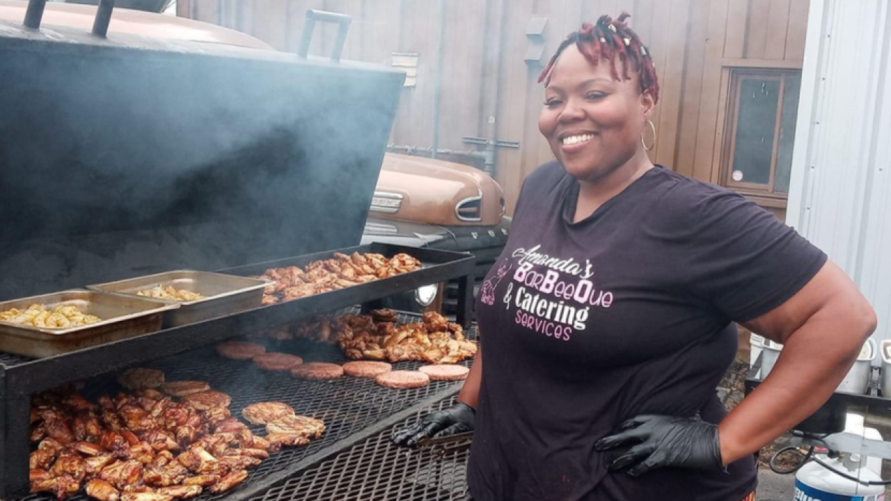 Amanda Kinsey-Joplin in a black t-shirt standing in front of a large barbecue smoker