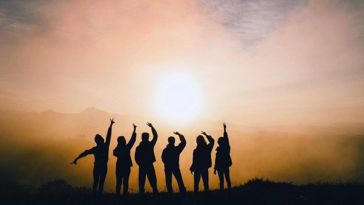 Six people in a row silhouetted against a sunset.
