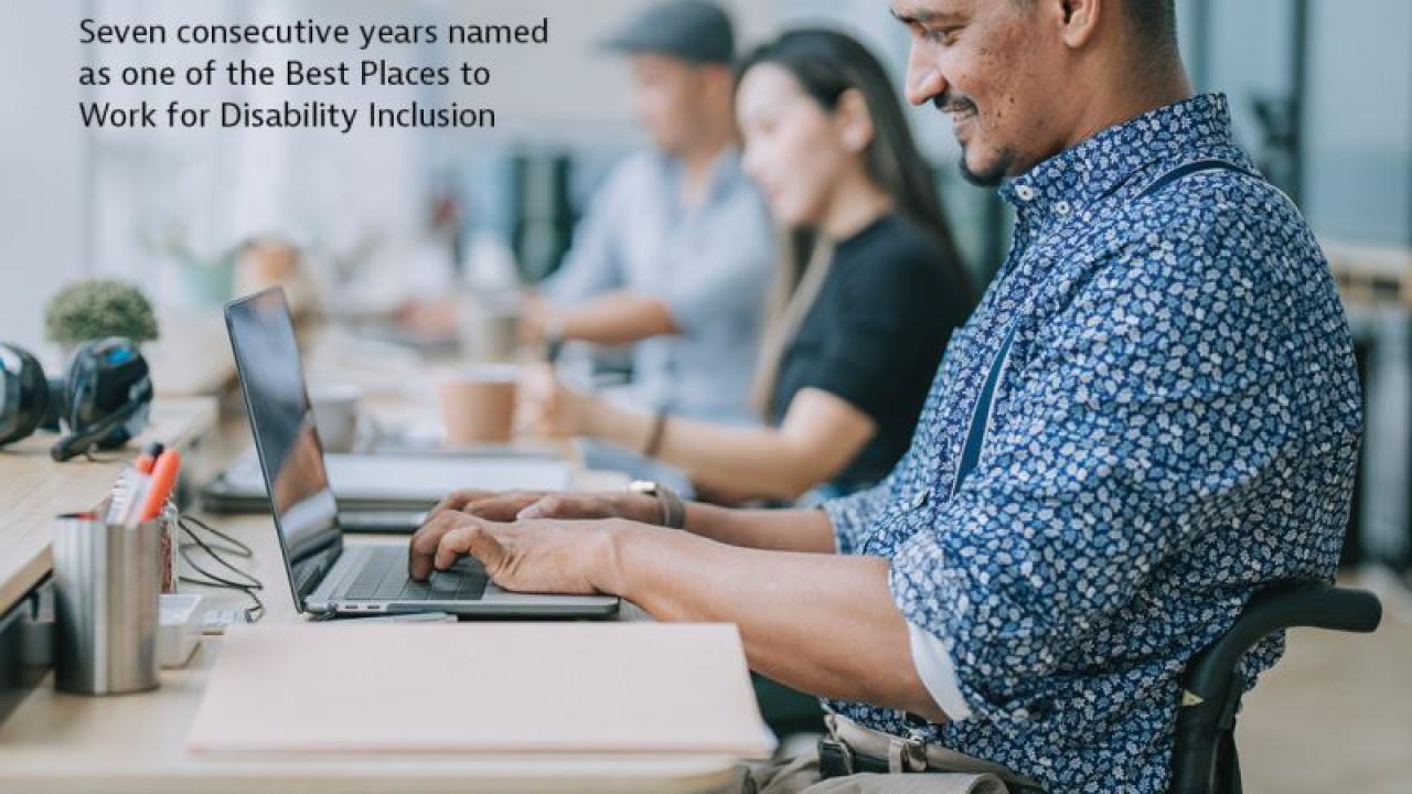 A person in a wheelchair at a desk working on a laptop. "We ar IN on advancing disability inclusion and equity."