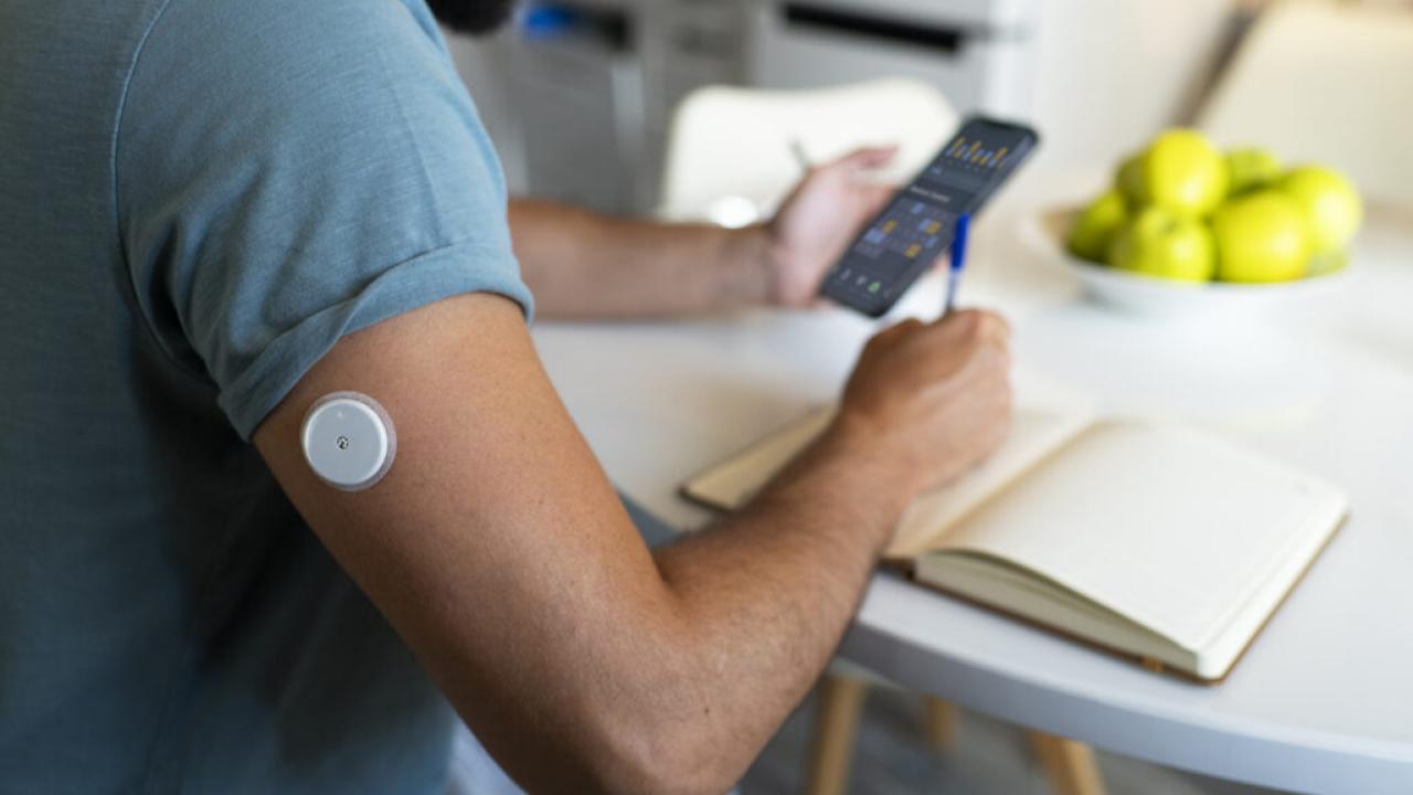Diabetic man checking glucose patch sensor.