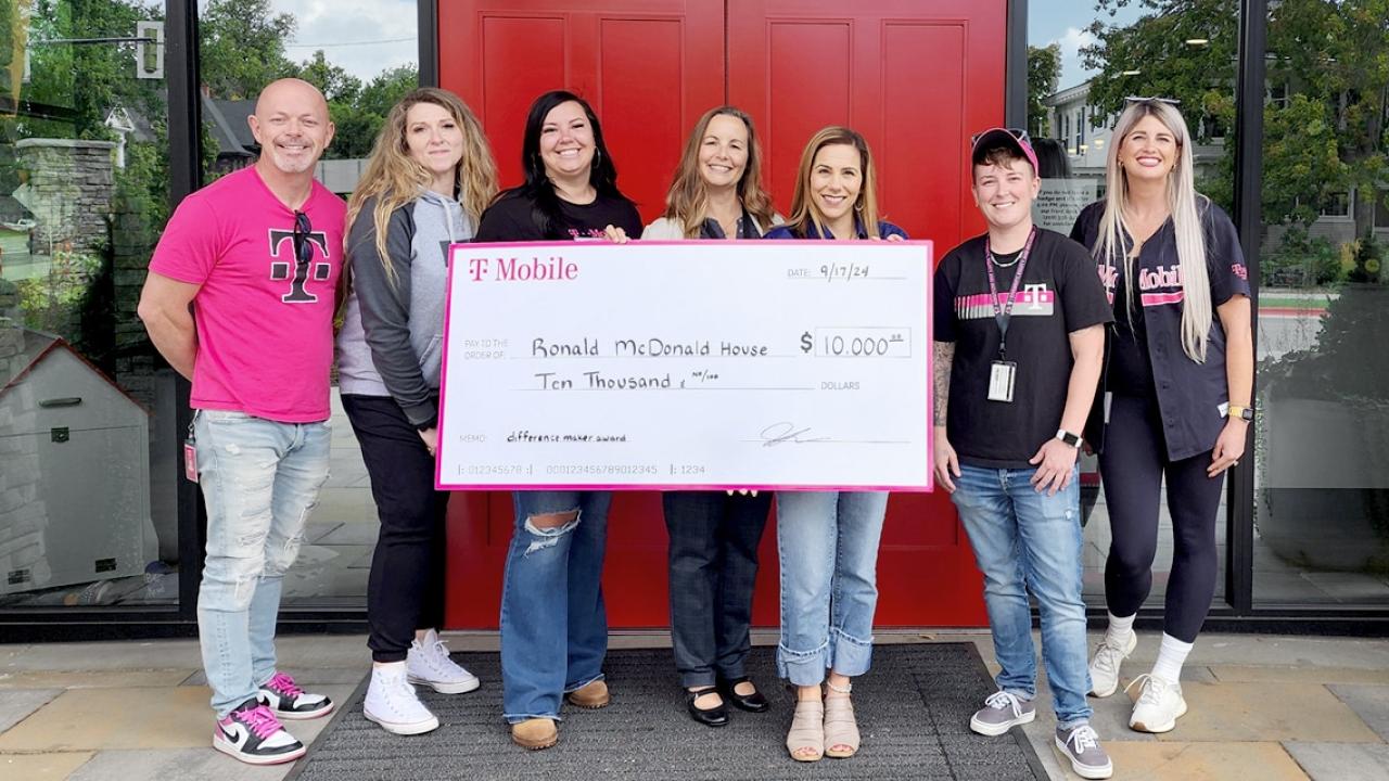 A small group posed with a large check outside a building